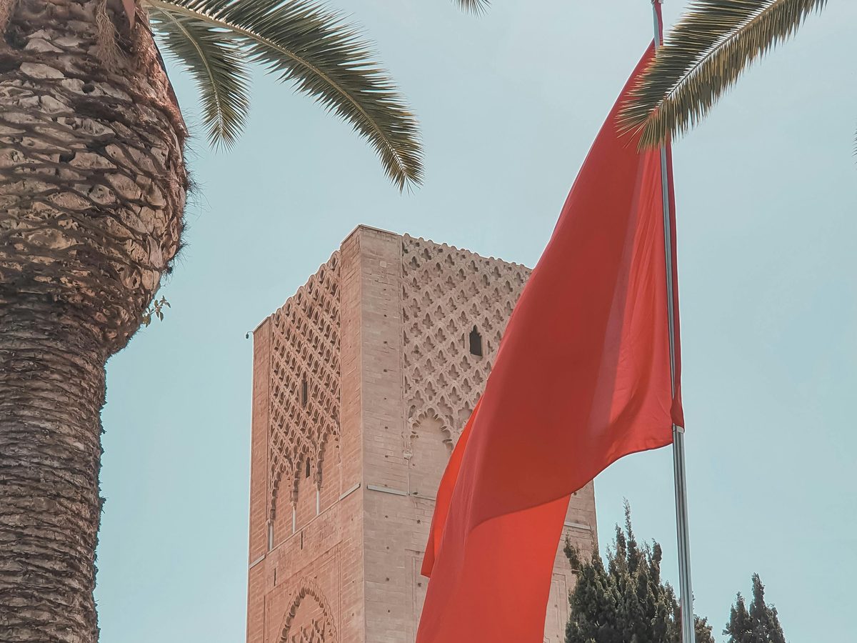 The Hassan Tower in Rabat with a Moroccan flag flying alongside, framed by palm fronds